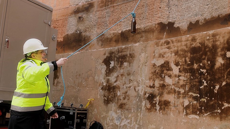 Kvinna i byggarbetskläder slänger glasflaska i en vägg. 