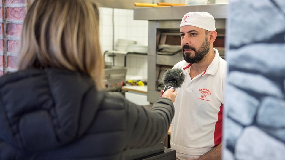 En kvinna intervjuar en manlig pizzabagare i en pizzeria.