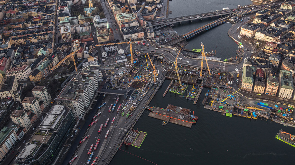 Flygfoto över Slussenområdet 2019. Vy från öst. Mellan Södermalm och Gamla stan pågår byggarbeten och åtta gula lyftkranar står på byggarbetsplatsen.