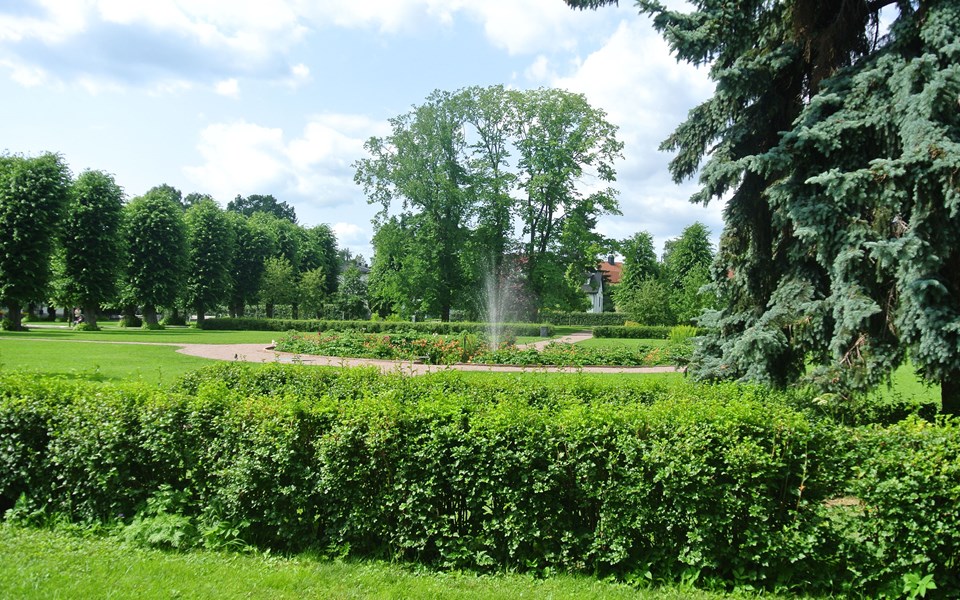 Lummig park med gräsytor, träd och buskar. I mitten finns en fontän, foto.