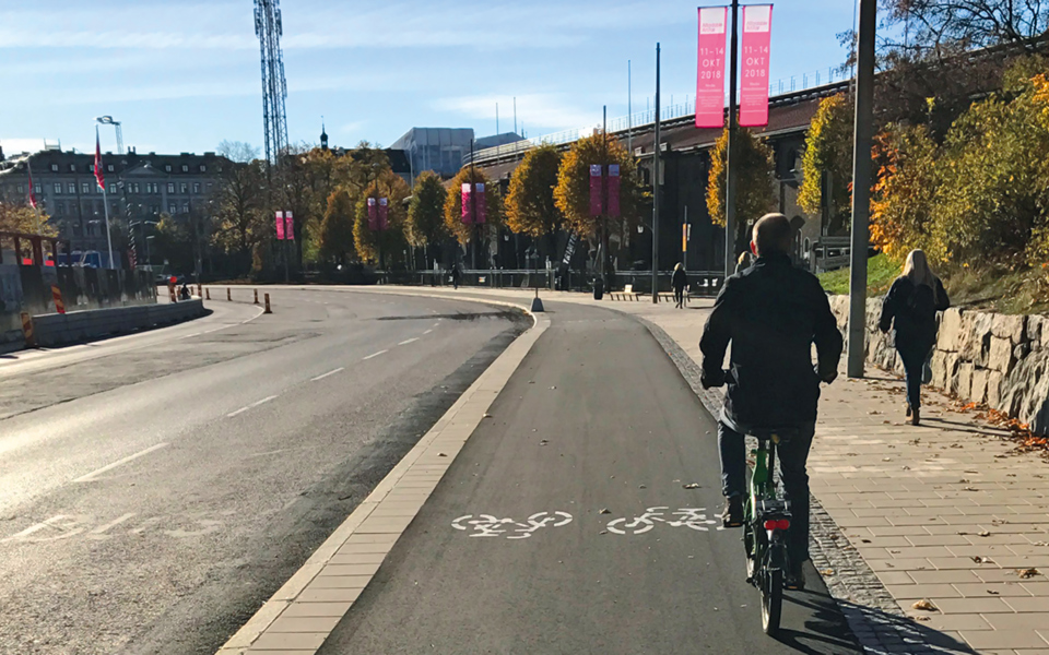 En cyklist cyklar på en cykelbanan utmed bilväg, foto.