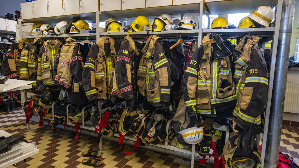 Brandmännens jackor byxor och hjälmar på en klädställning, foto. 