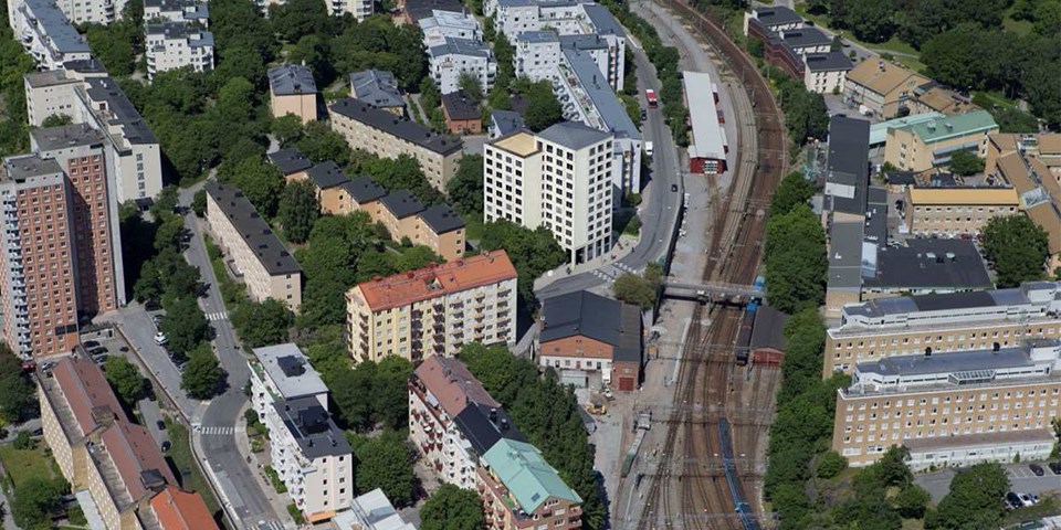 Flygfotografi över ett område med flerbostadshus och järnvägsspår.