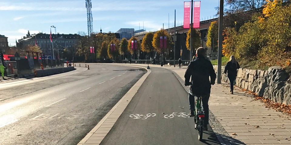 En cyklist cyklar på en cykelbanan utmed bilväg, foto.